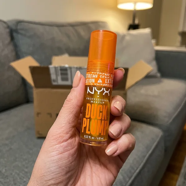 Foto de la clienta: mano sujetando el gloss con la caja del envío al fondo